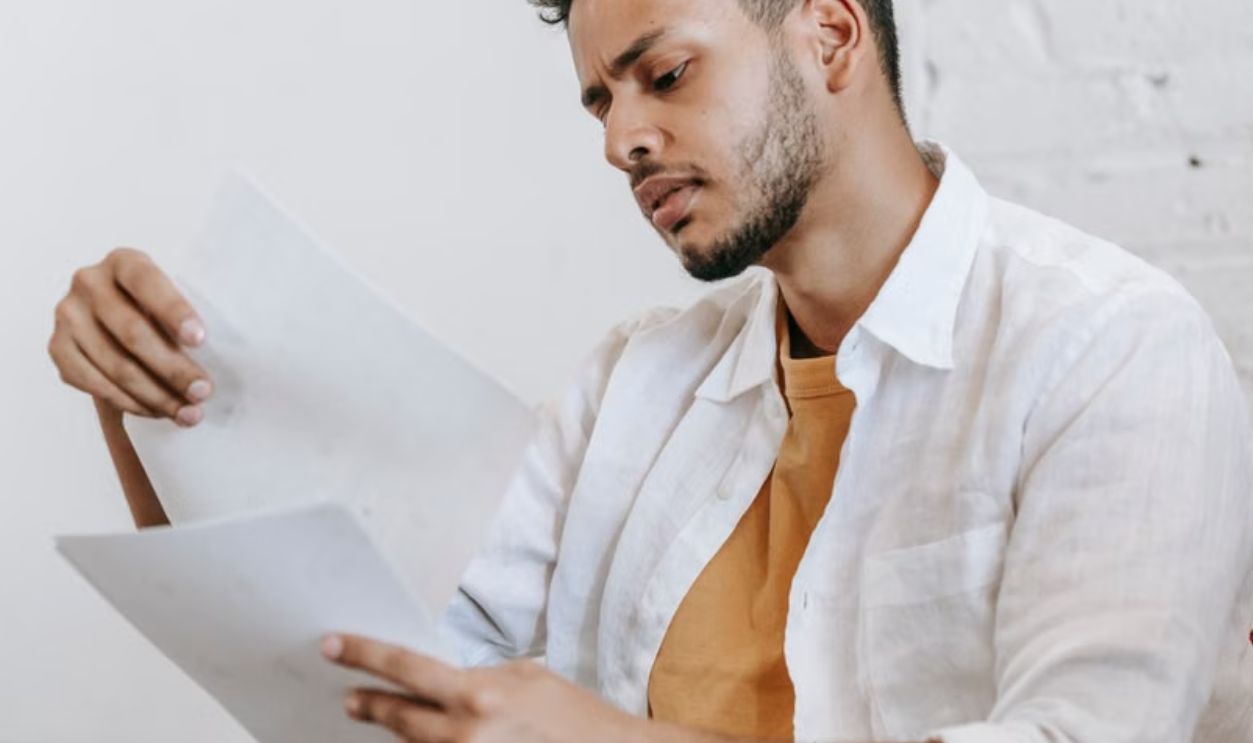 A man in a white shirt sitting on a couch, deeply focused on reading documents