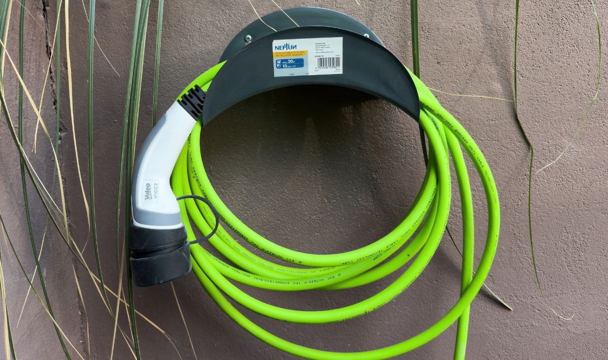 Paris, France - May 12, 2025: A bright green electric vehicle charging cable with a Type 2 Valeo connector is neatly wrapped and mounted on a Neptun wall holder attached to a textured exterior wall