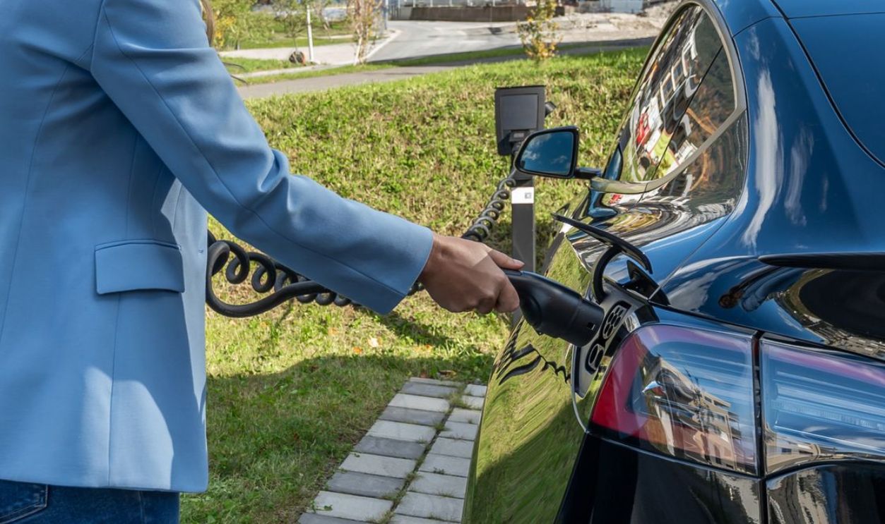 Person connecting an electric car to a charging station outdoors, showcasing green energy transition