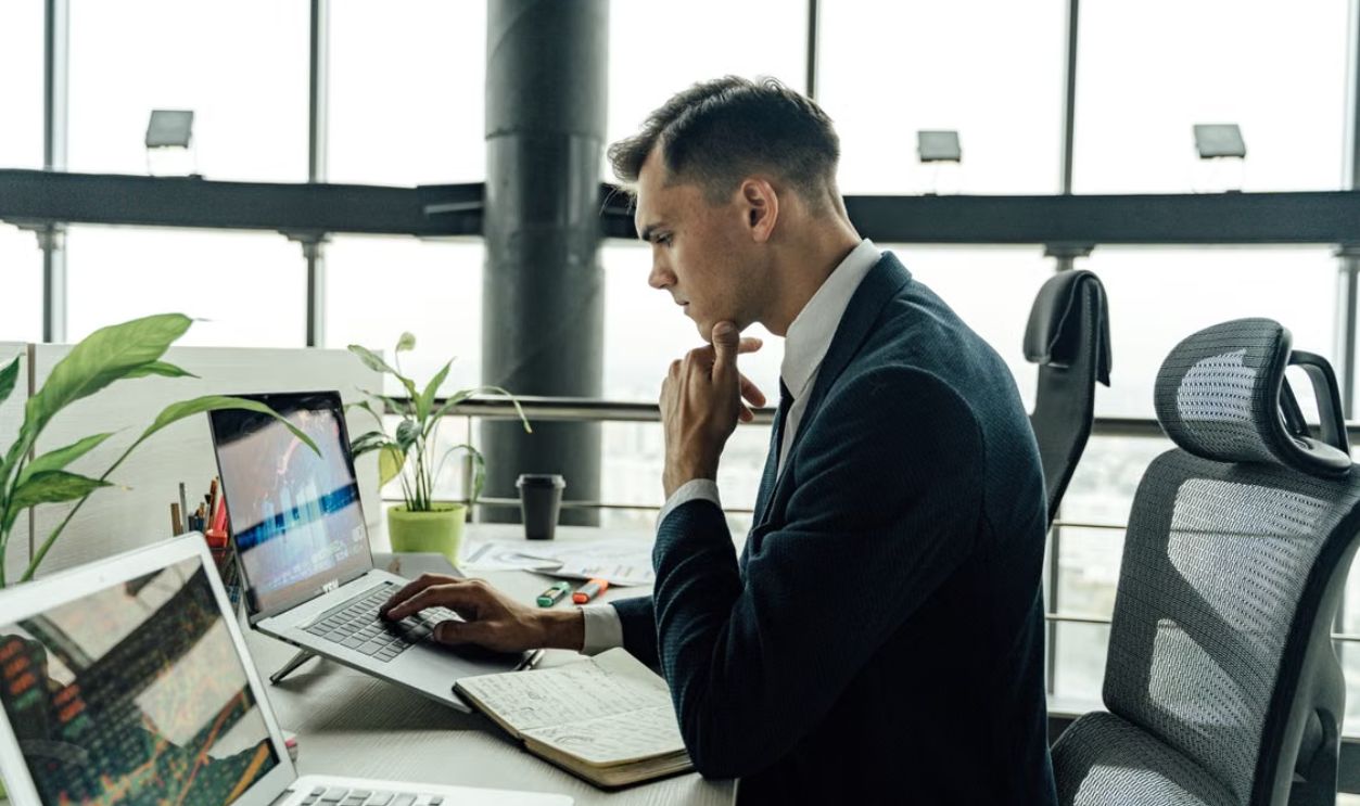 Professional man analyzing stock market data at modern office workspace with laptops