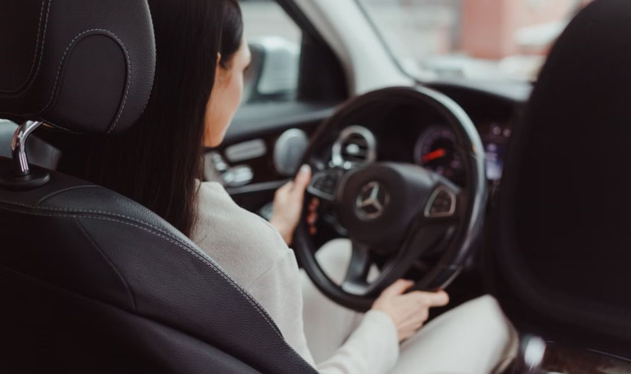 Rear view of a woman driving a Mercedes Benz, focusing on the interior and steering wheel