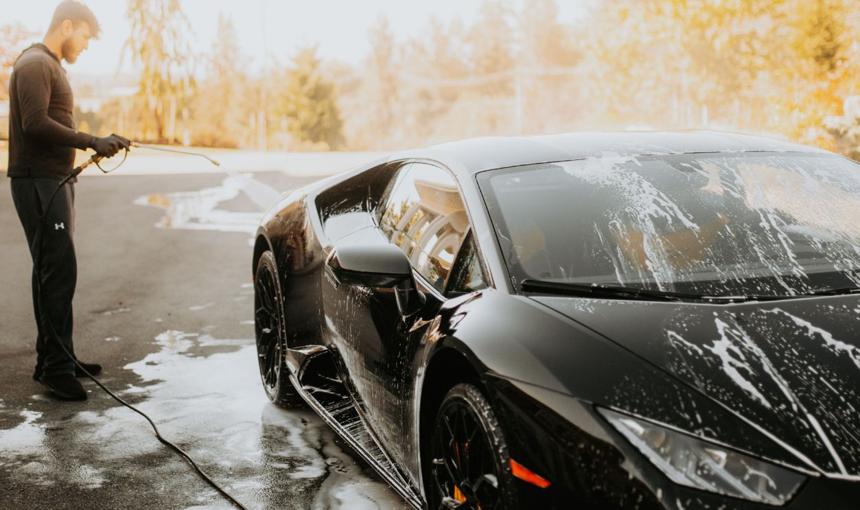 A man washing a sleek black Lamborghini sports car with soap suds