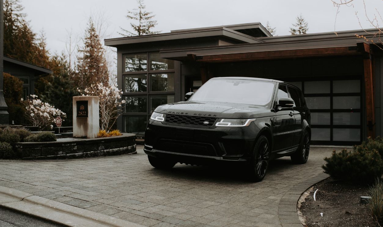 A sleek black luxury SUV parked in front of a modern home with glass facade