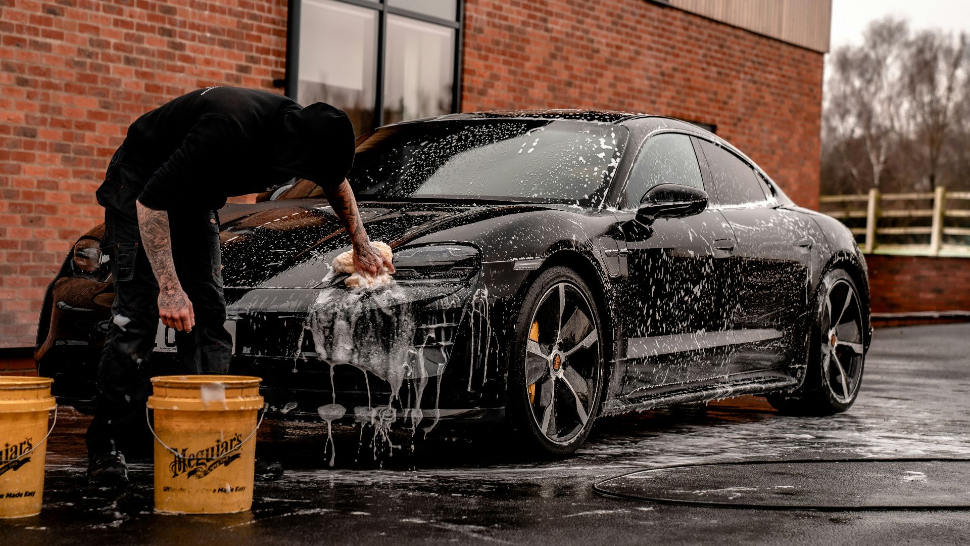 man in black t-shirt and black pants doing water splash on black coupe during daytime