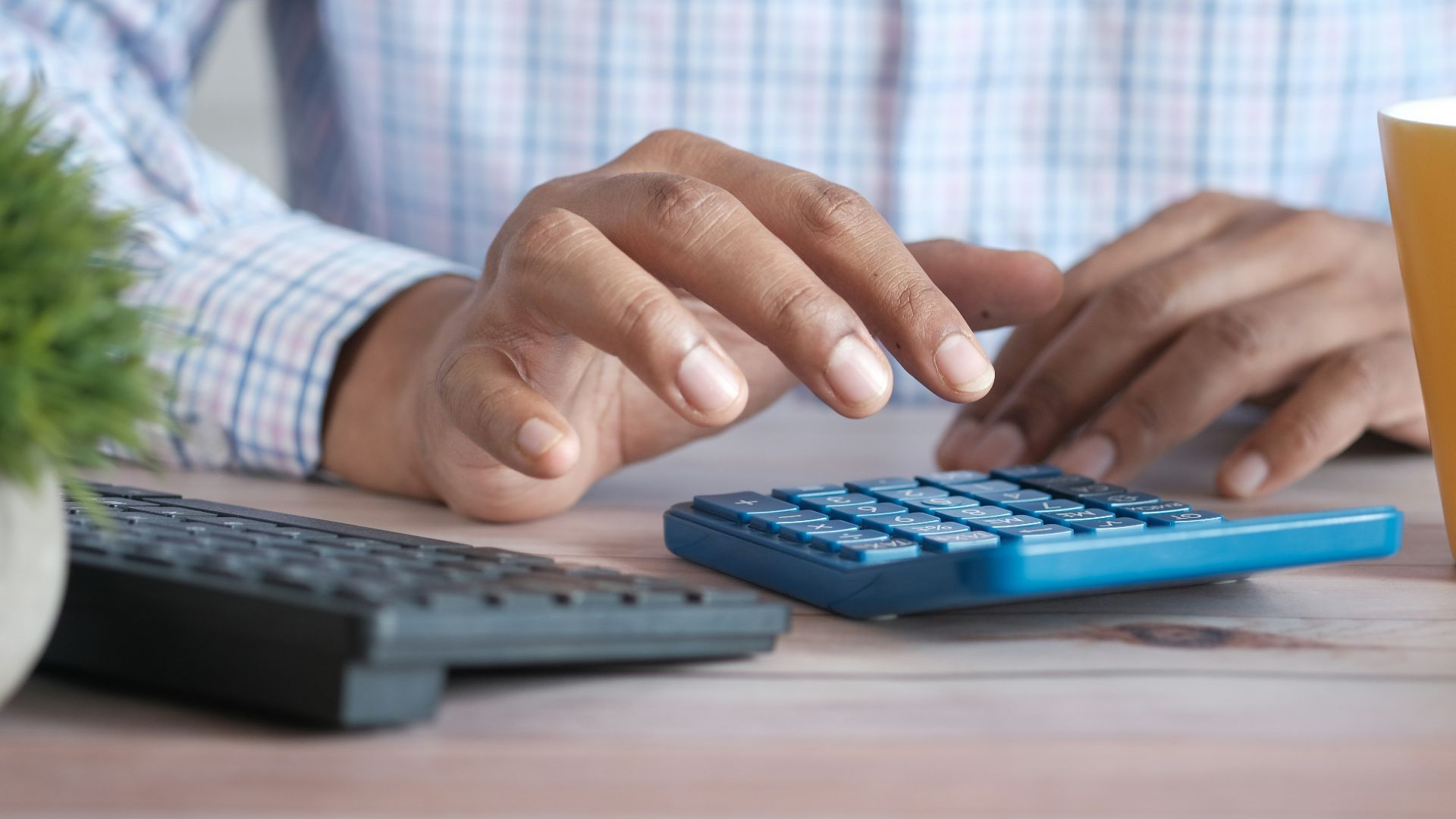 person using calculator at desk with coffee mug