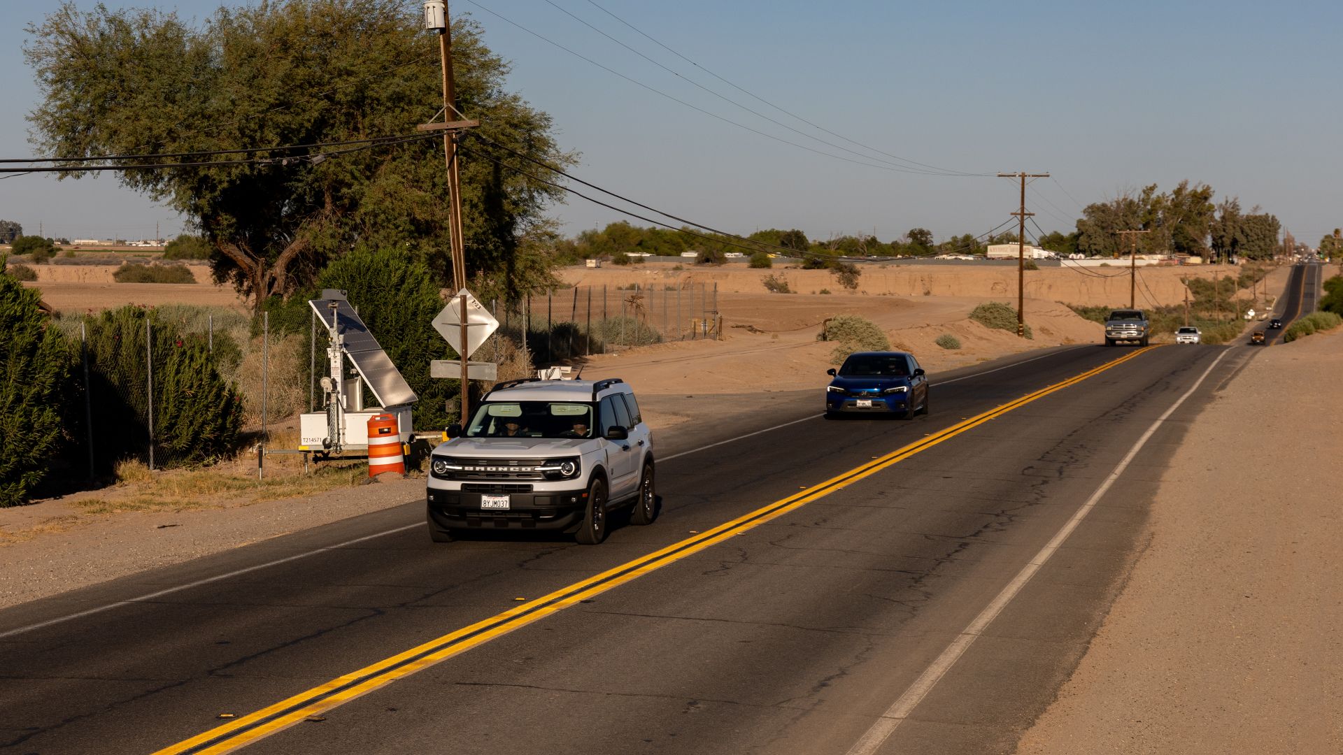Two automated license plate reader (ALPR) systems—one disguised as a construction barrel and surveilling westbound traffic, the other held aloft in a metal box on the trailer beside it and surveilling eastbound traffic—on the north side of California Stat