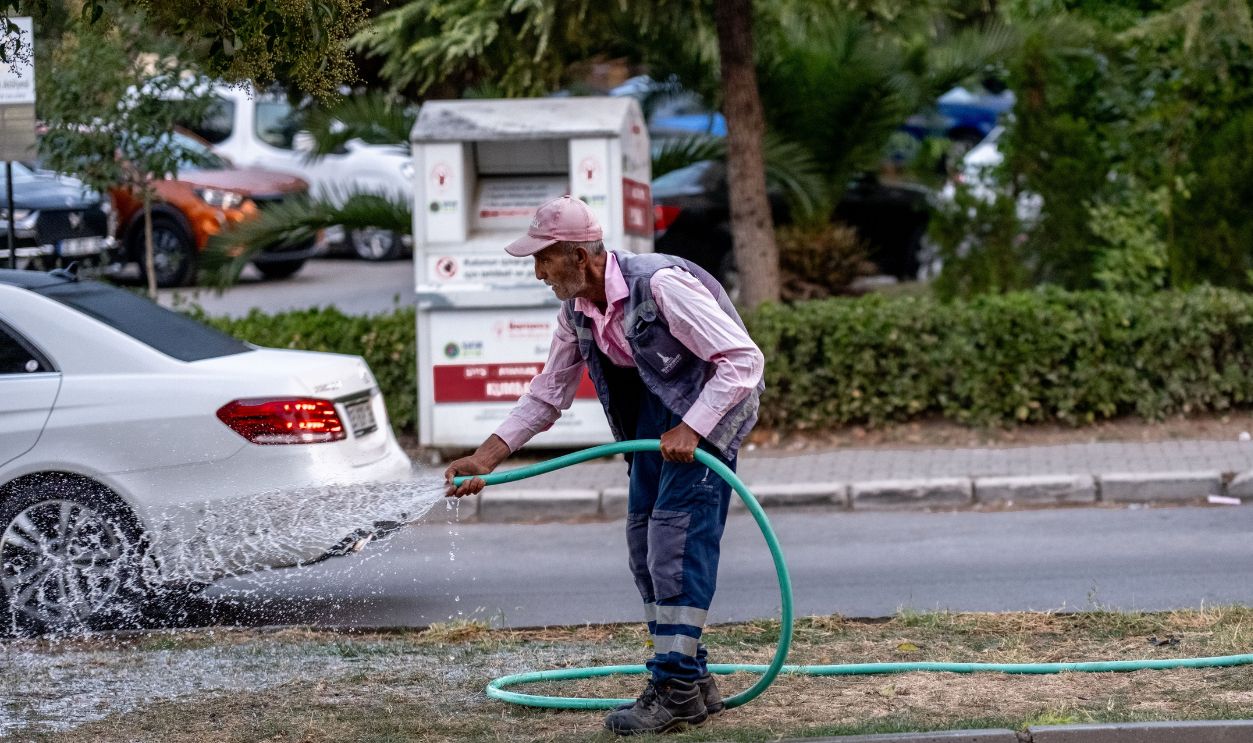 Senior man in work clothes watering grass on a street in İzmir, Turkiye