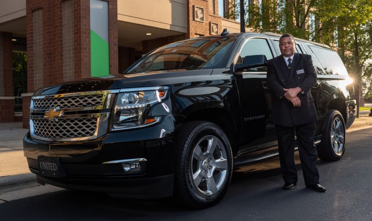 Chauffeur standing confidently next to a black SUV, offering luxury transportation service