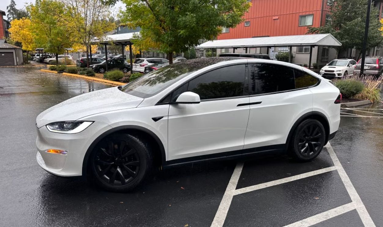 A sleek white electric SUV with tinted windows is parked in a Seattle neighborhood on a rainy fall day