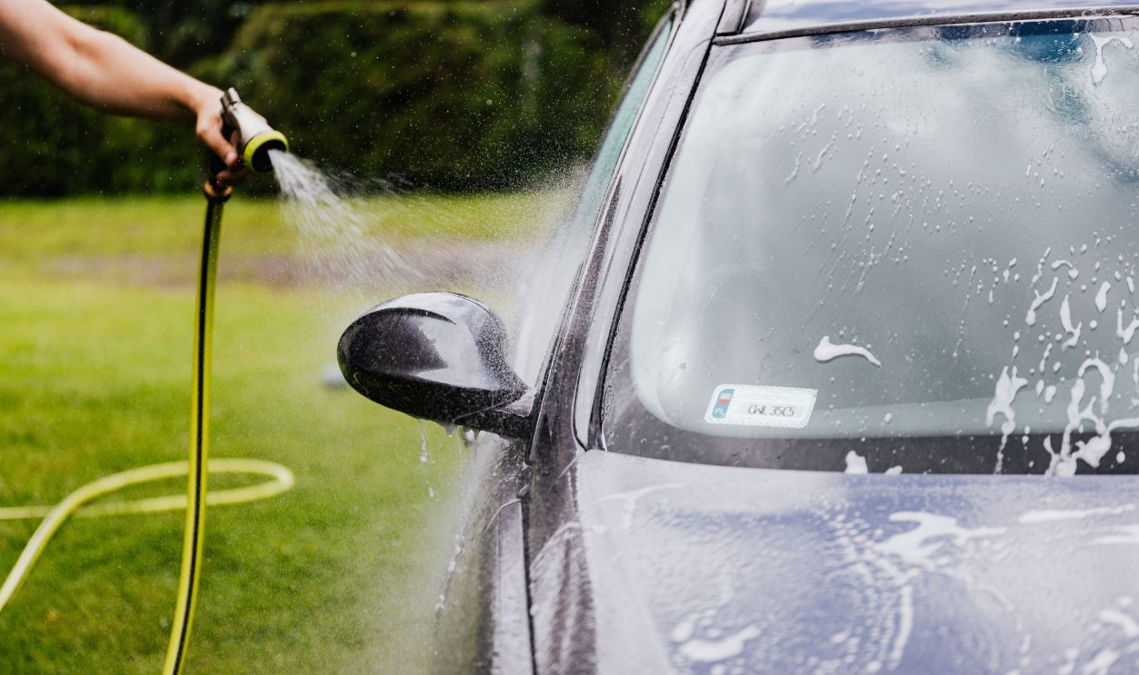 Person washing a car with a hose outdoors, creating suds