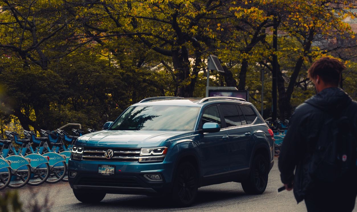 Volkswagen SUV driving in a city with a pedestrian walking by trees and buildings