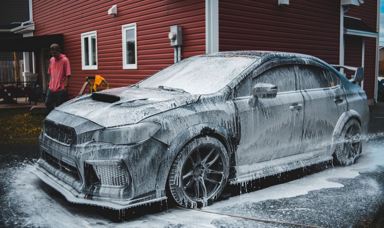 A luxury sports car covered in foam during a wash outside a suburban