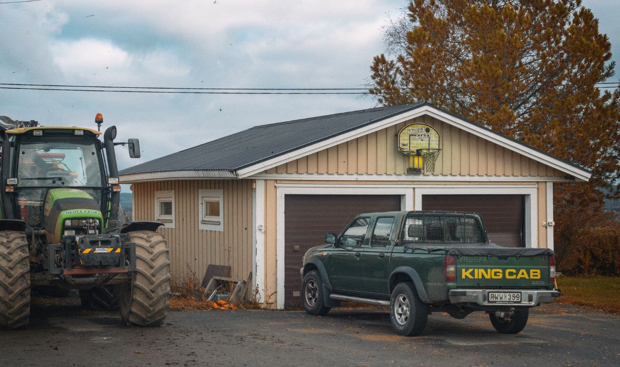 A rural scene in Hedenaset, Sweden featuring a tractor and King Cab pickup truck parked by a garage
