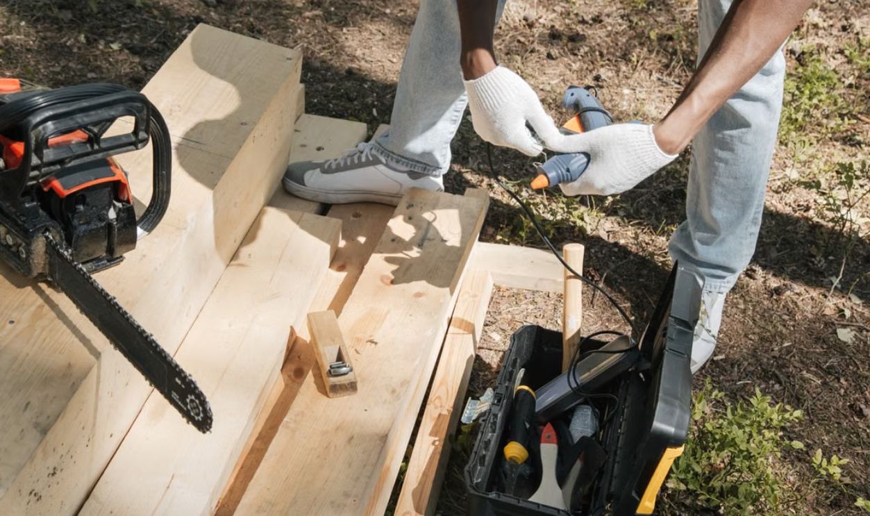 A carpenter using power tools to work on a wooden panel outdoors, showcasing construction and craftsmanship