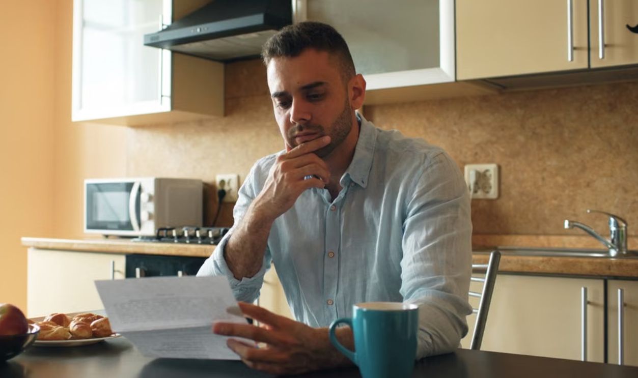 Thoughtful man reads a letter in a cozy kitchen setting with sunlight