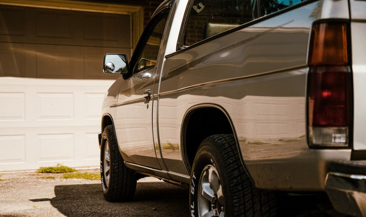 A silver pickup truck parked in a sunny residential driveway with closed garage doors