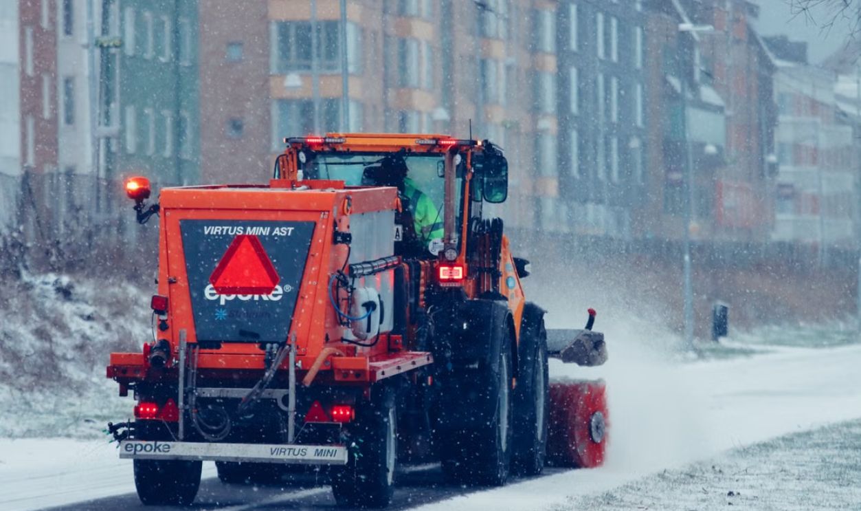 Orange snowplow in action clearing a snow-covered street during a winter snowfall.