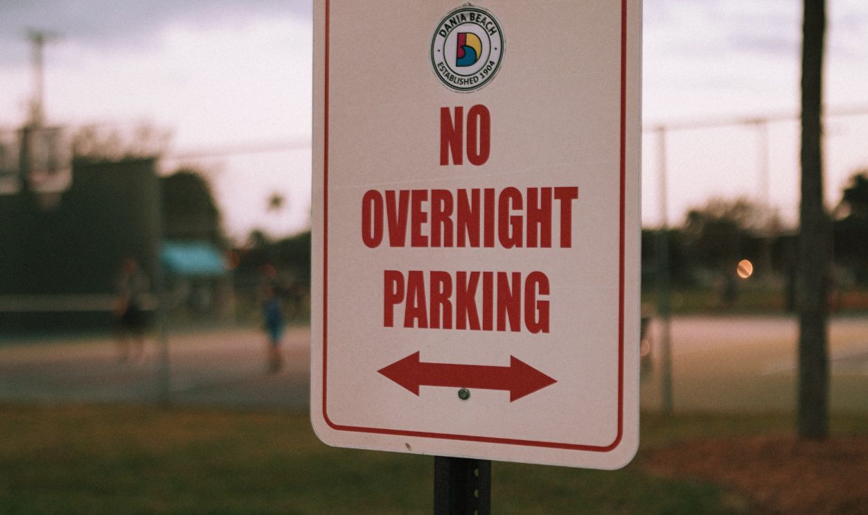 A 'No Overnight Parking' sign photographed in an urban park during daytime.