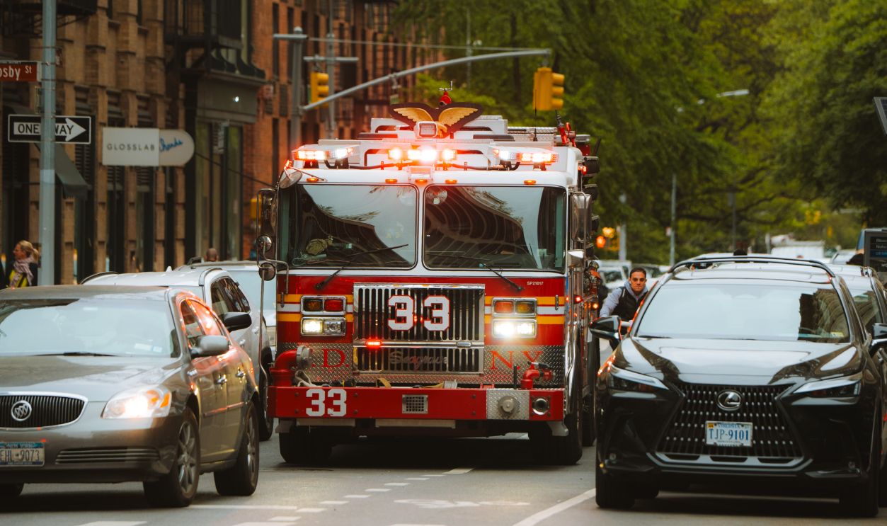 Firetruck rushing through urban New York City street amidst traffic.