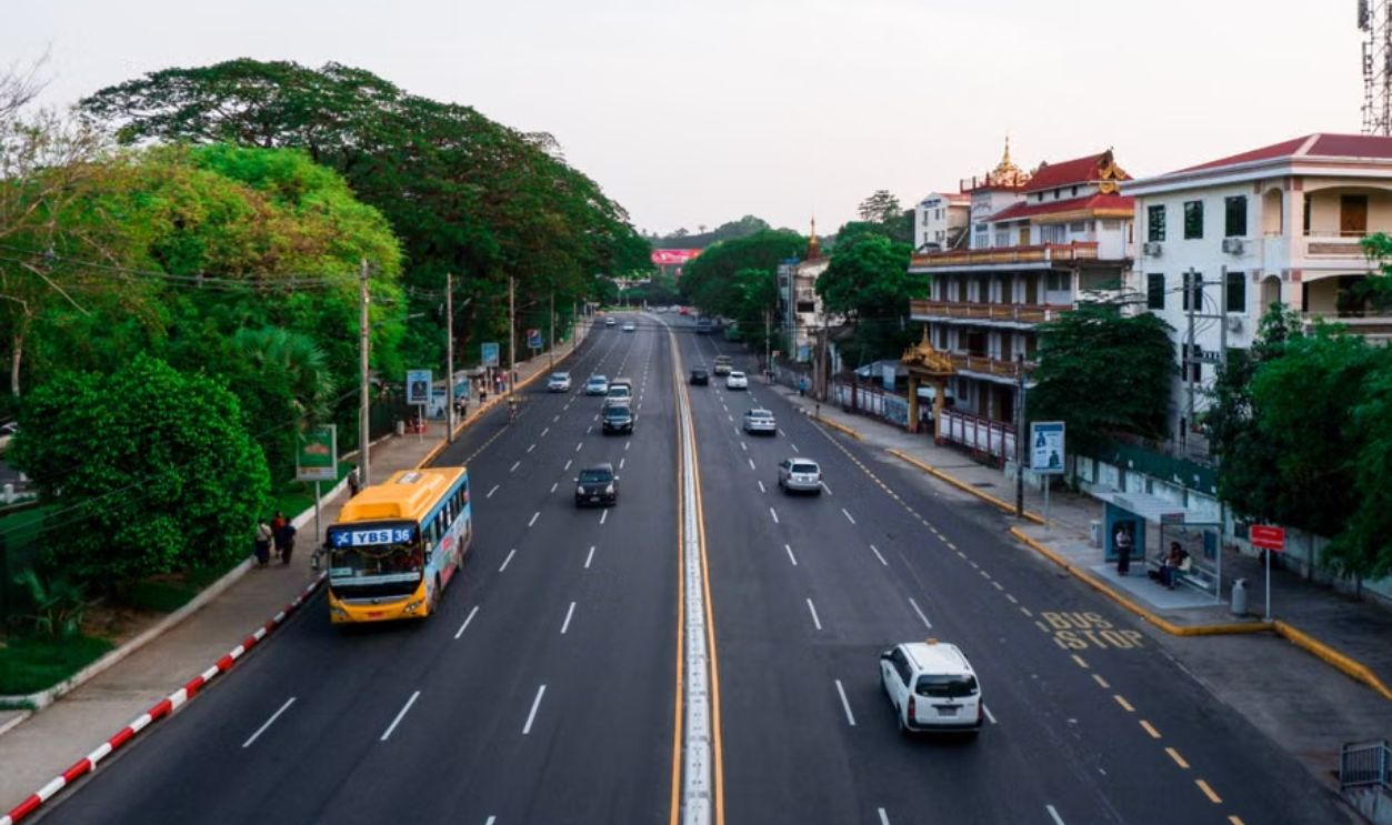 Wide view of a city street lined with trees and buildings, showcasing daytime urban traffic.
