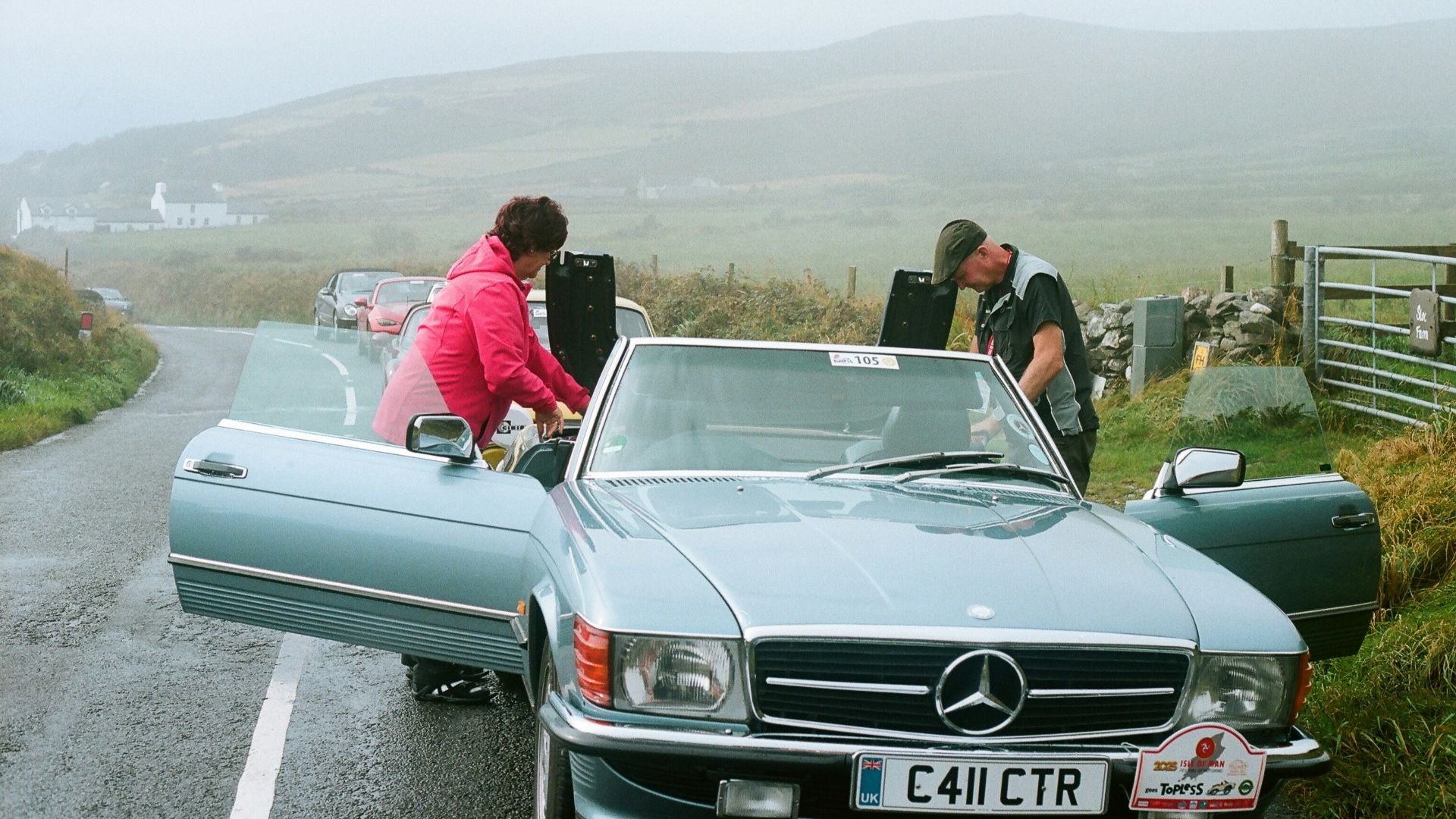 Two people loading items into a vintage convertible car.