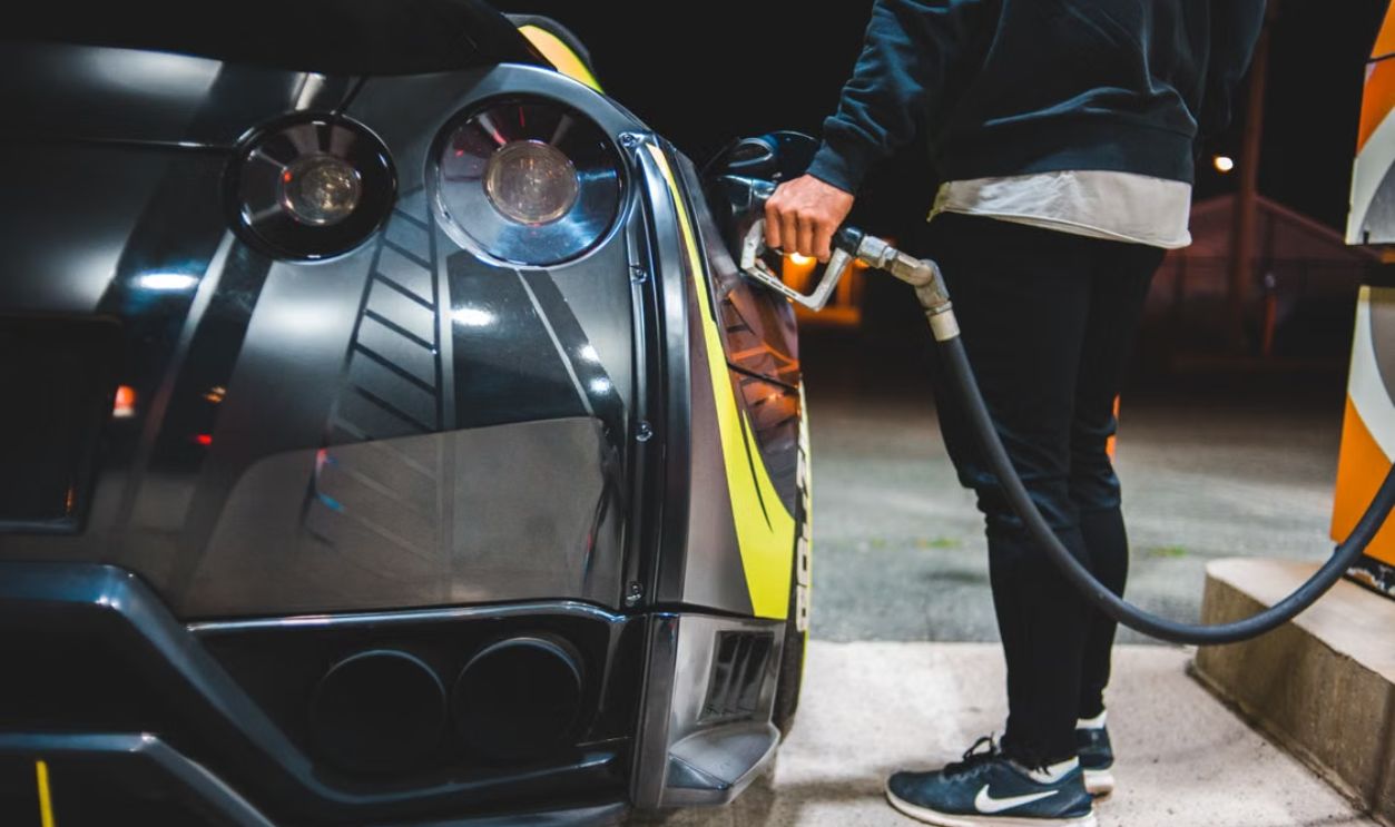 Man refuels sleek sports car under twilight at urban gas station