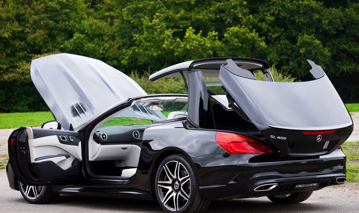 Black luxury convertible car with open roof in a green outdoor setting.