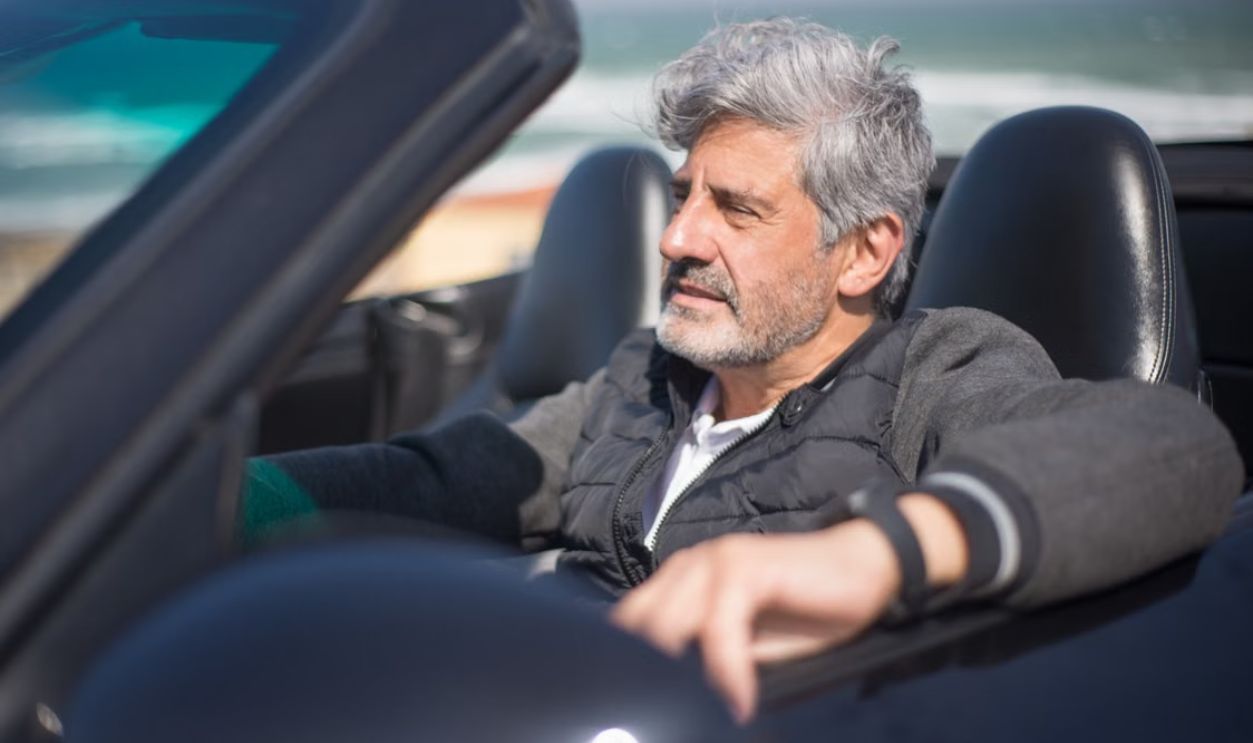 Senior man enjoying a road trip along a scenic coastal drive in a convertible car