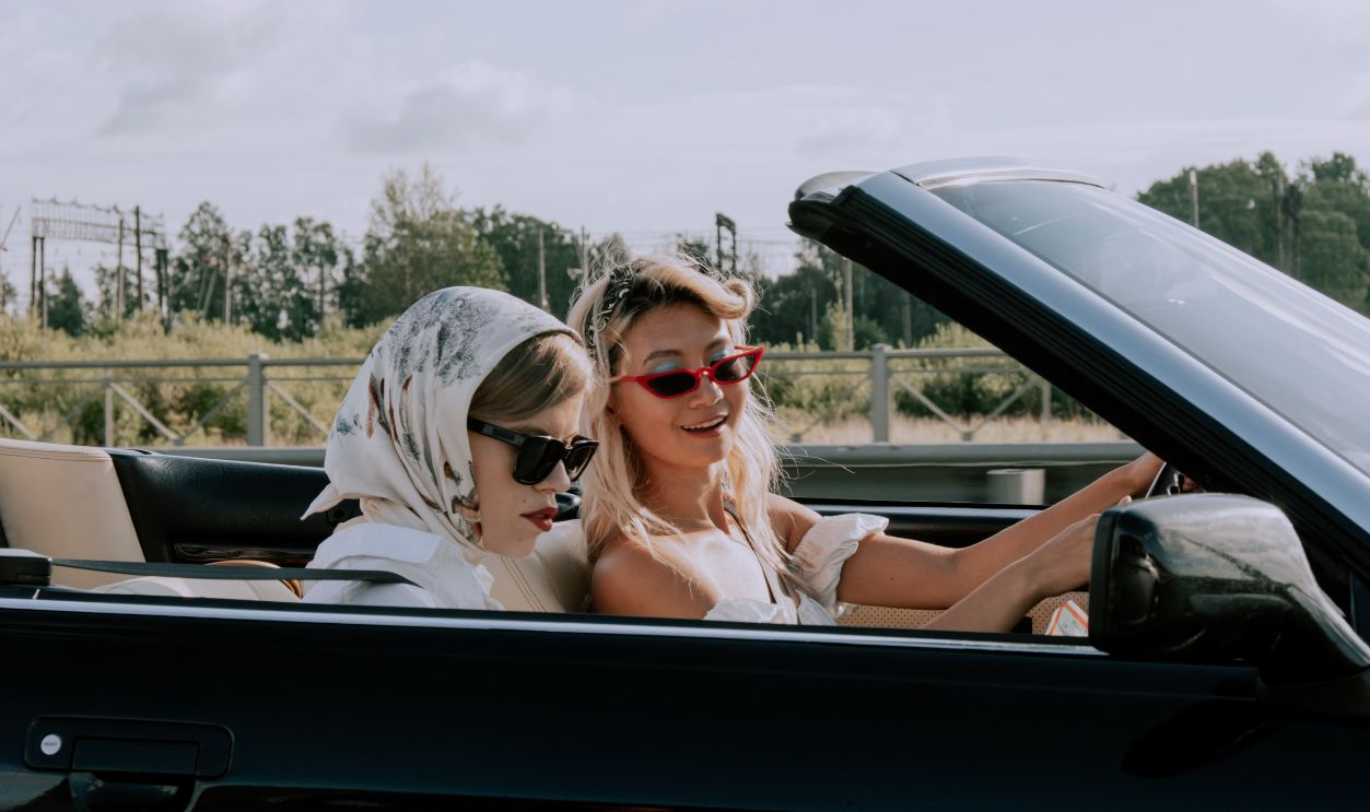 Two stylish women driving a convertible car outdoors, enjoying the sunny day with fashionable sunglasses