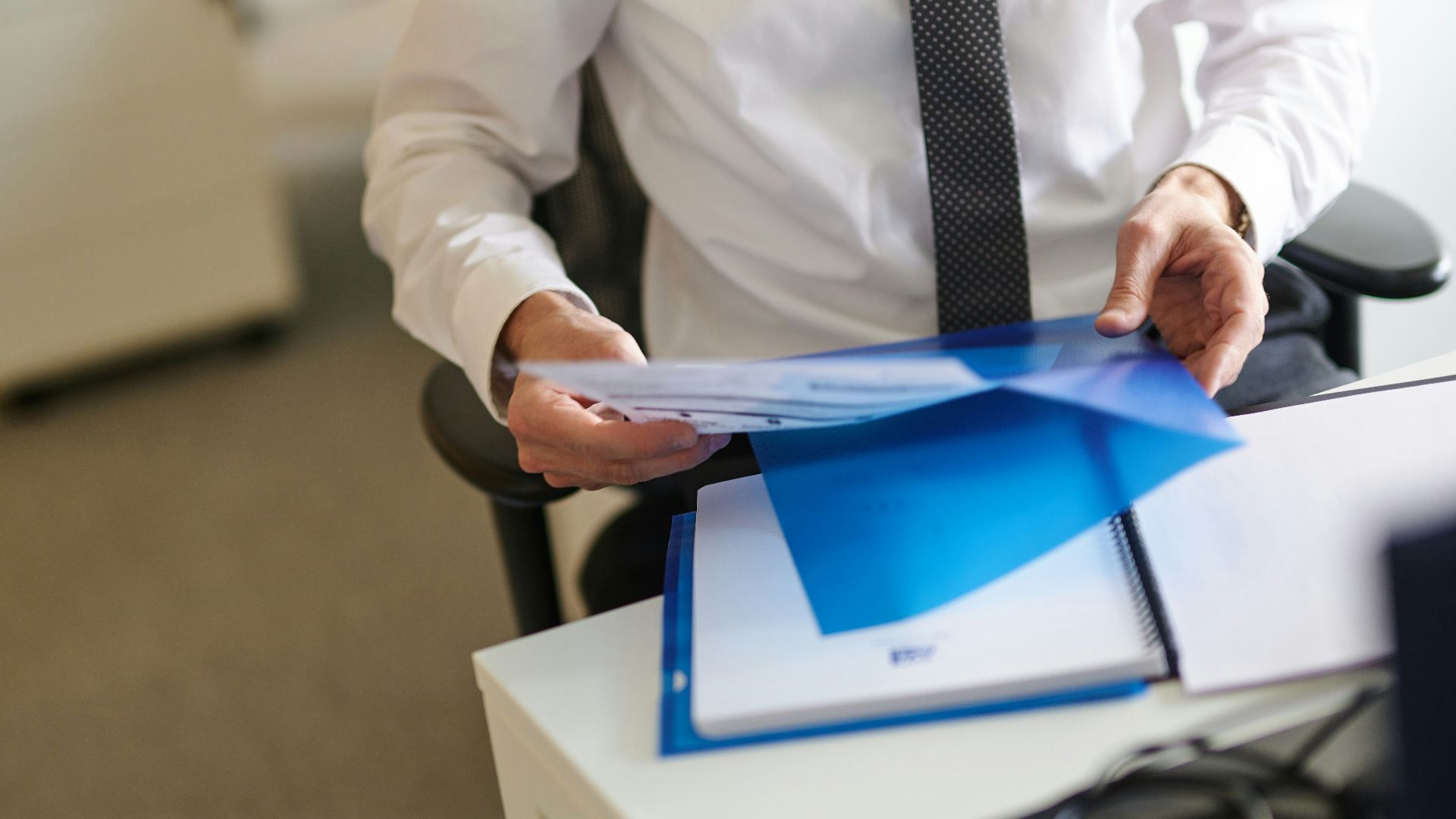 a man in a white shirt and tie holding a folder