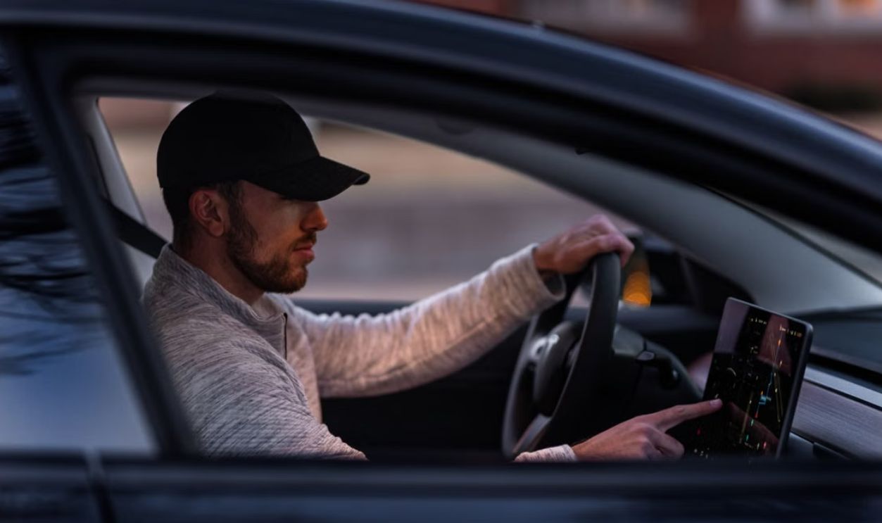 A man interacts with a touchscreen inside an electric car, driving through Dallas, TX