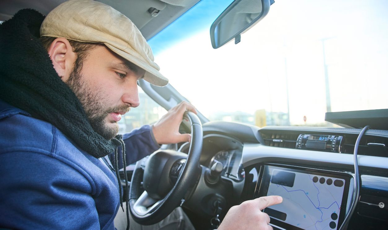 A man who, before starting to drive, locates his position and destination on a map on the screen in his car. Concept: the use of technology as a tool to help travelers.