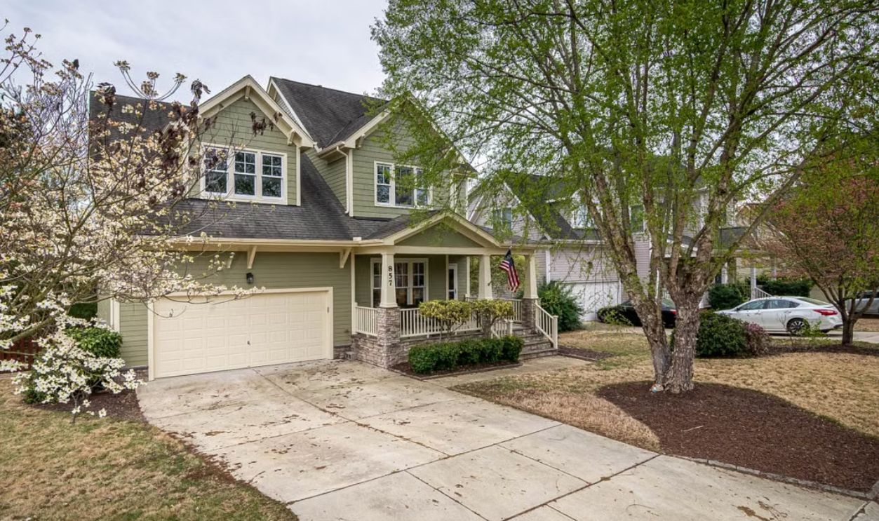 A picturesque suburban home with a lush front yard, driveway, and trees.