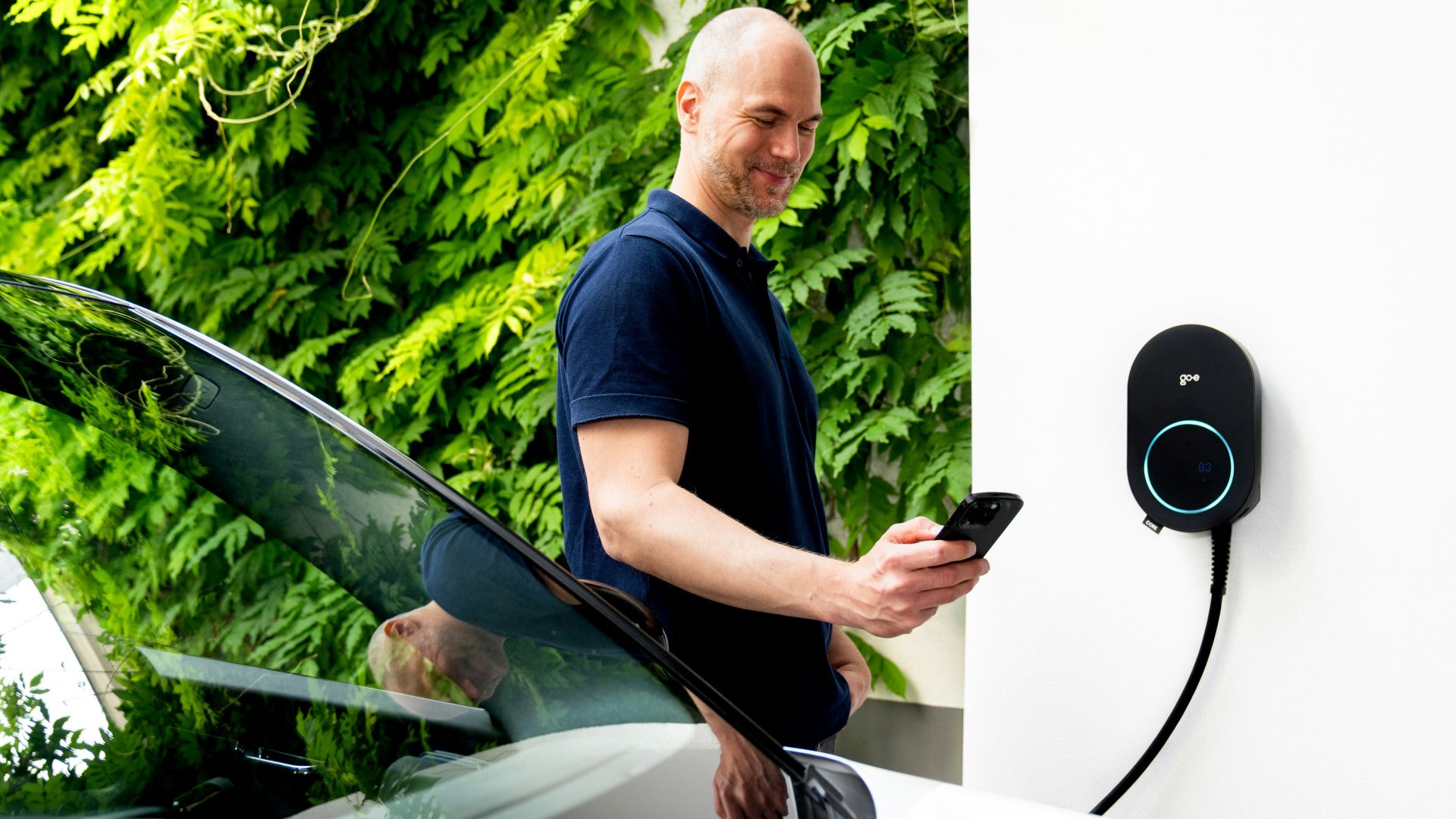 Man using phone near electric car charging station.