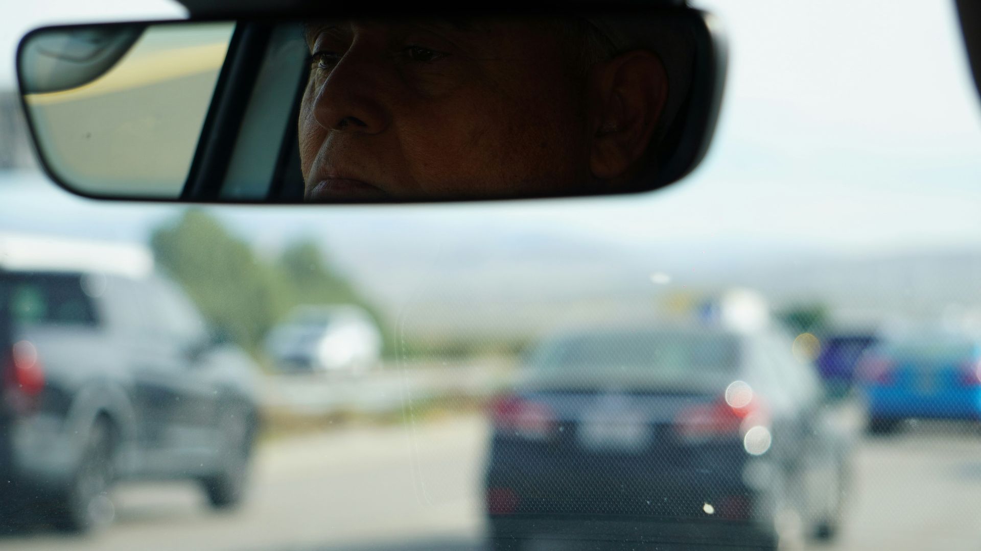 Driver's reflection visible in rearview mirror during traffic.
