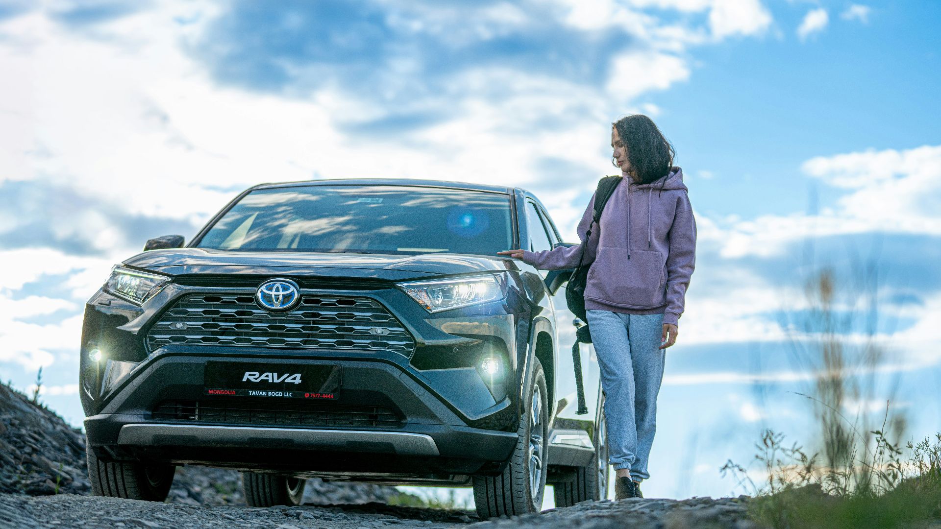 A woman standing next to a car on a dirt road