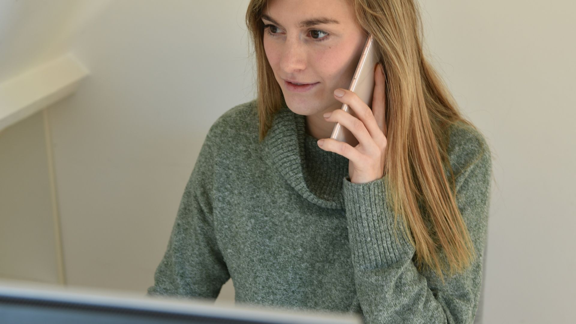 a woman sitting in front of a computer talking on a cell phone