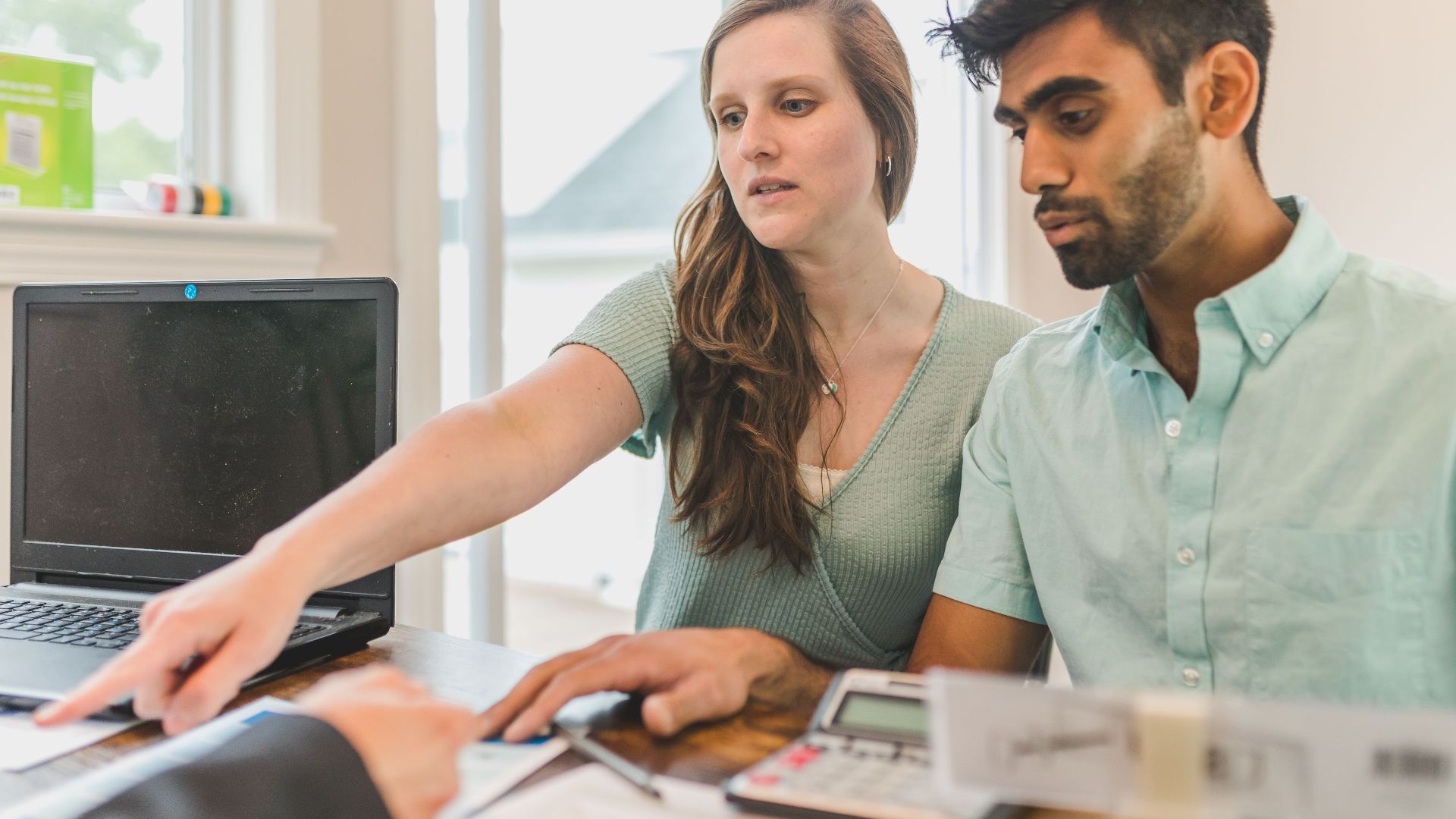 A young couple reviewing real estate documents with an advisor in a bright office.