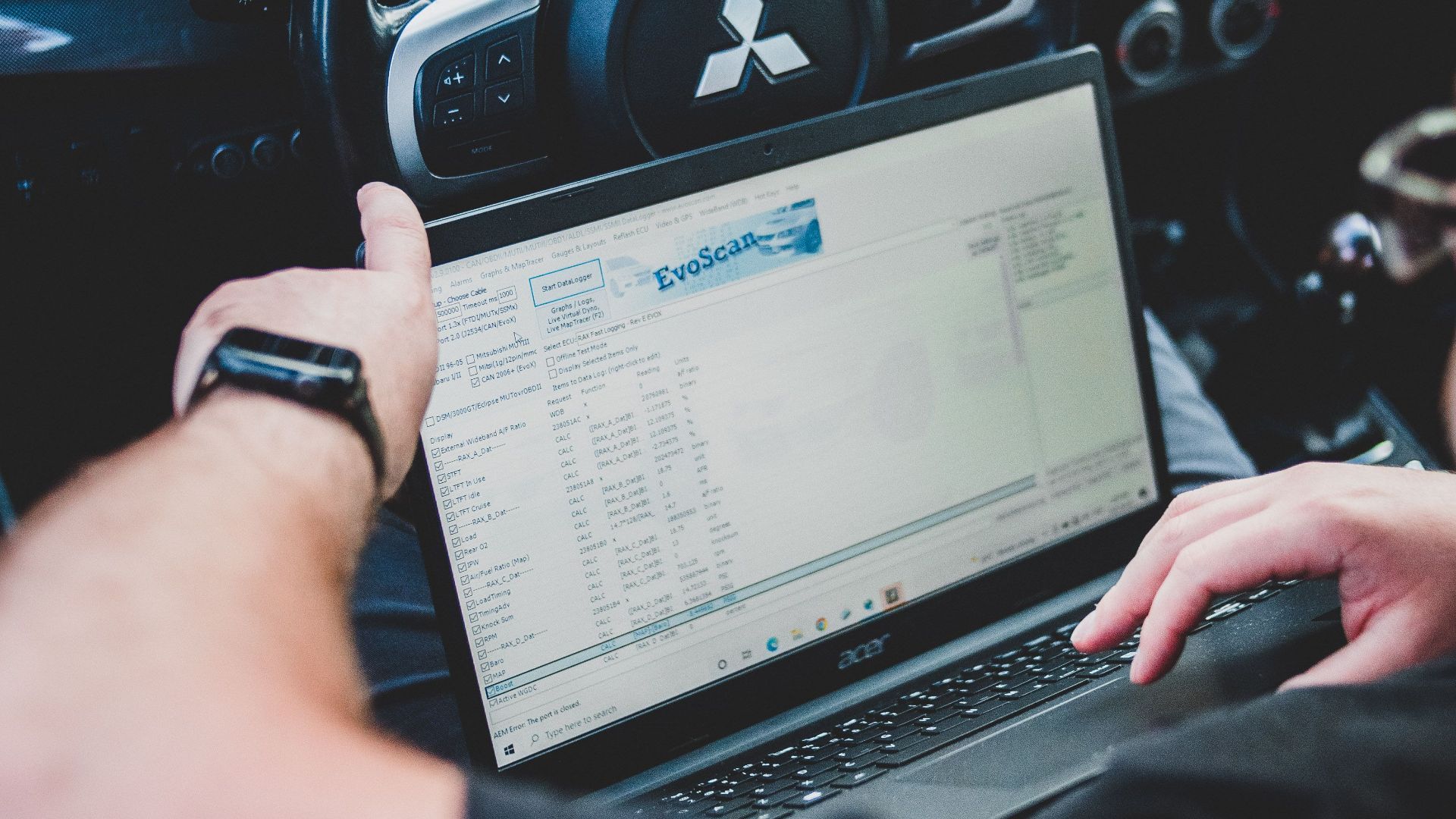 A person using a laptop inside a car for vehicle diagnostics, showcasing technology integration in automotive settings.