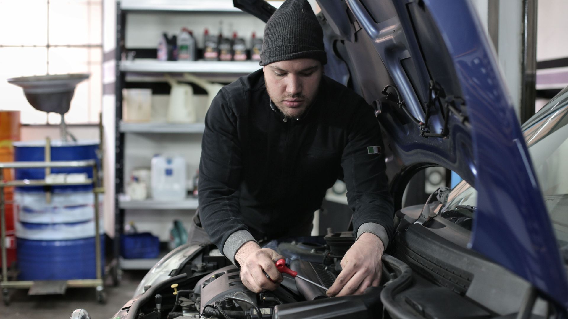 Man working under car hood in a garage, focused on engine repair