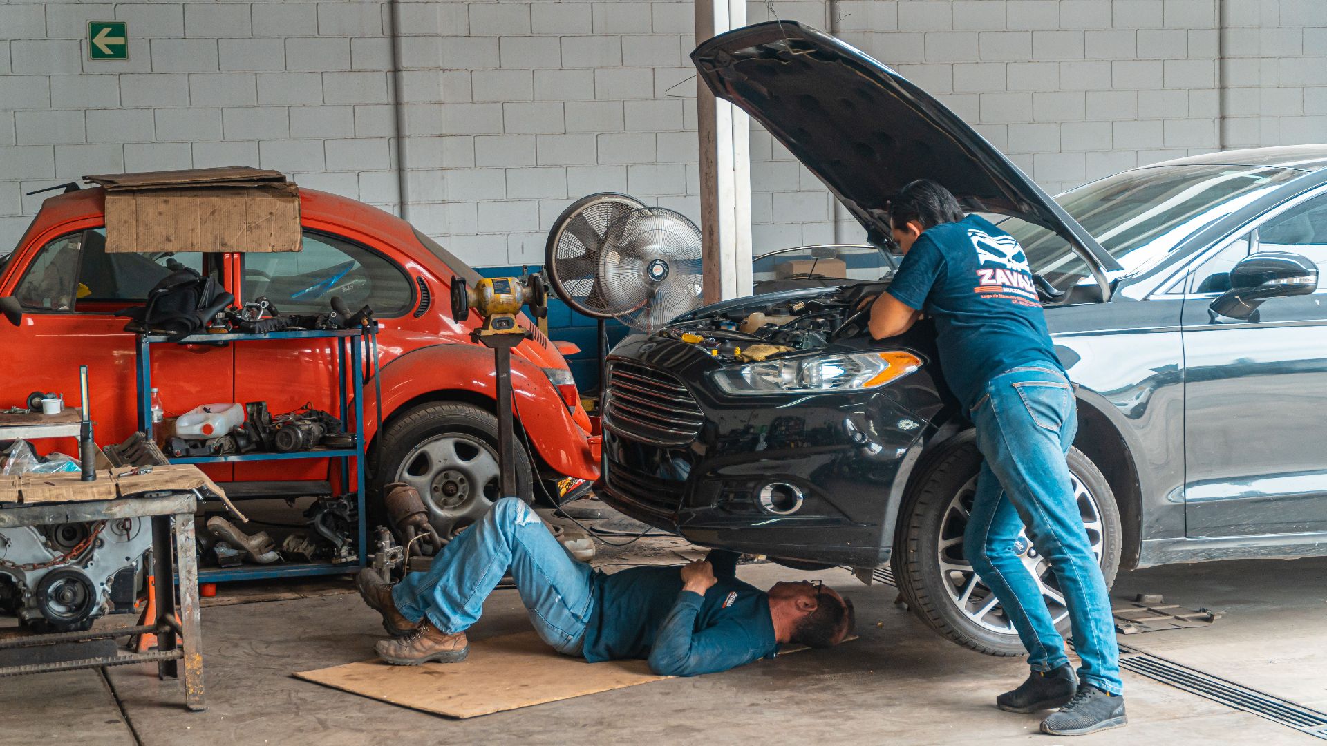Mechanics working in an automotive workshop, repairing cars and performing maintenance.