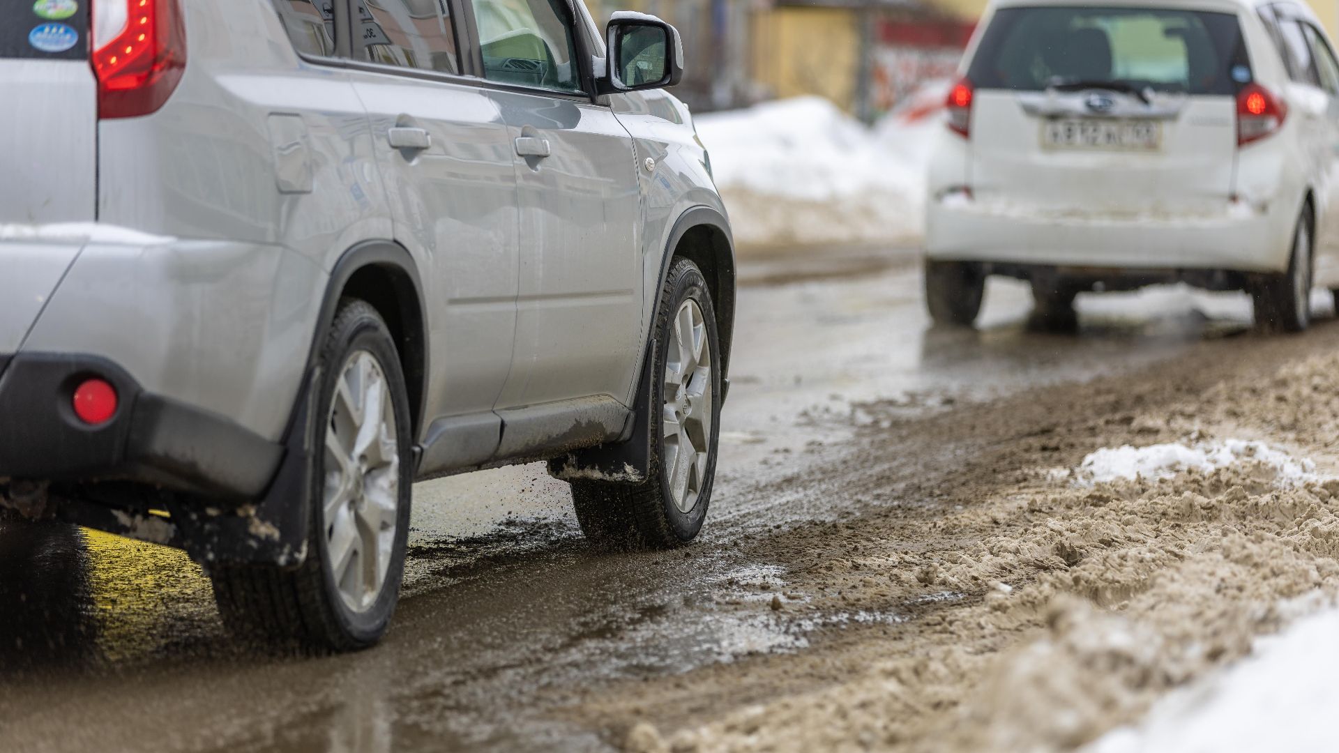 Two cars driving cautiously on a slushy, snowy road during winter.
