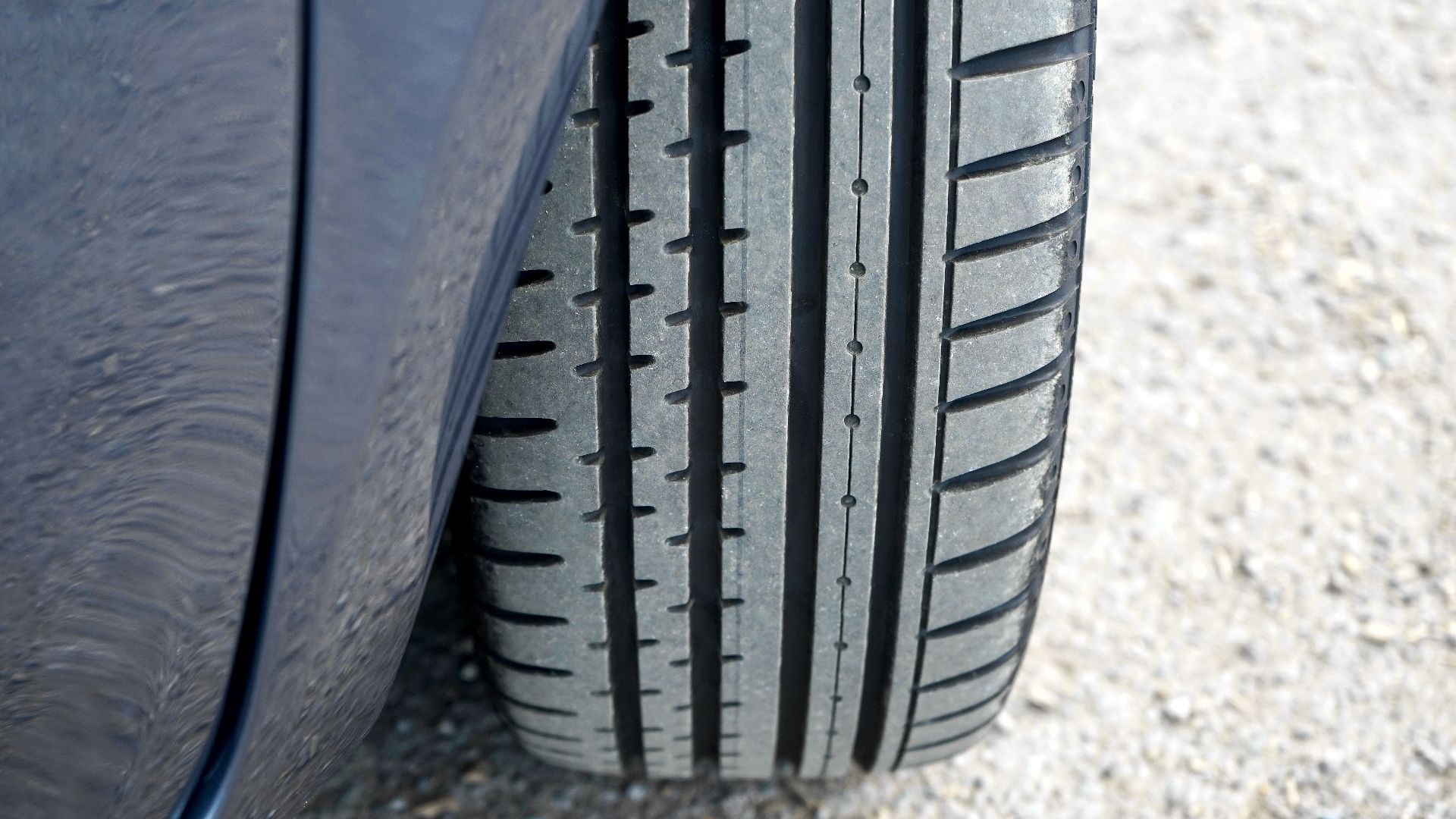 Detailed close-up of a car tire on a gravel road in natural light.
