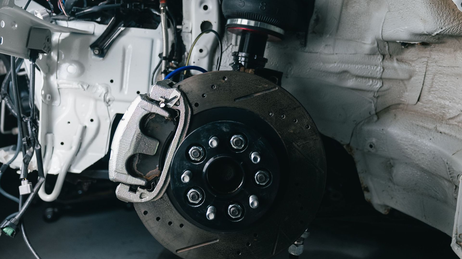 Close-up shot of a vehicle's suspension and brake assembly in a garage setting.