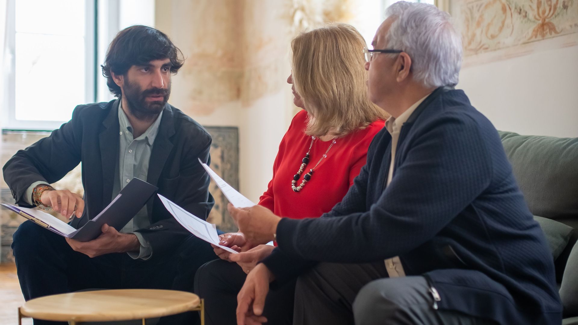 An advisor discussing financial documents with a senior couple indoors in a cozy living room setting.