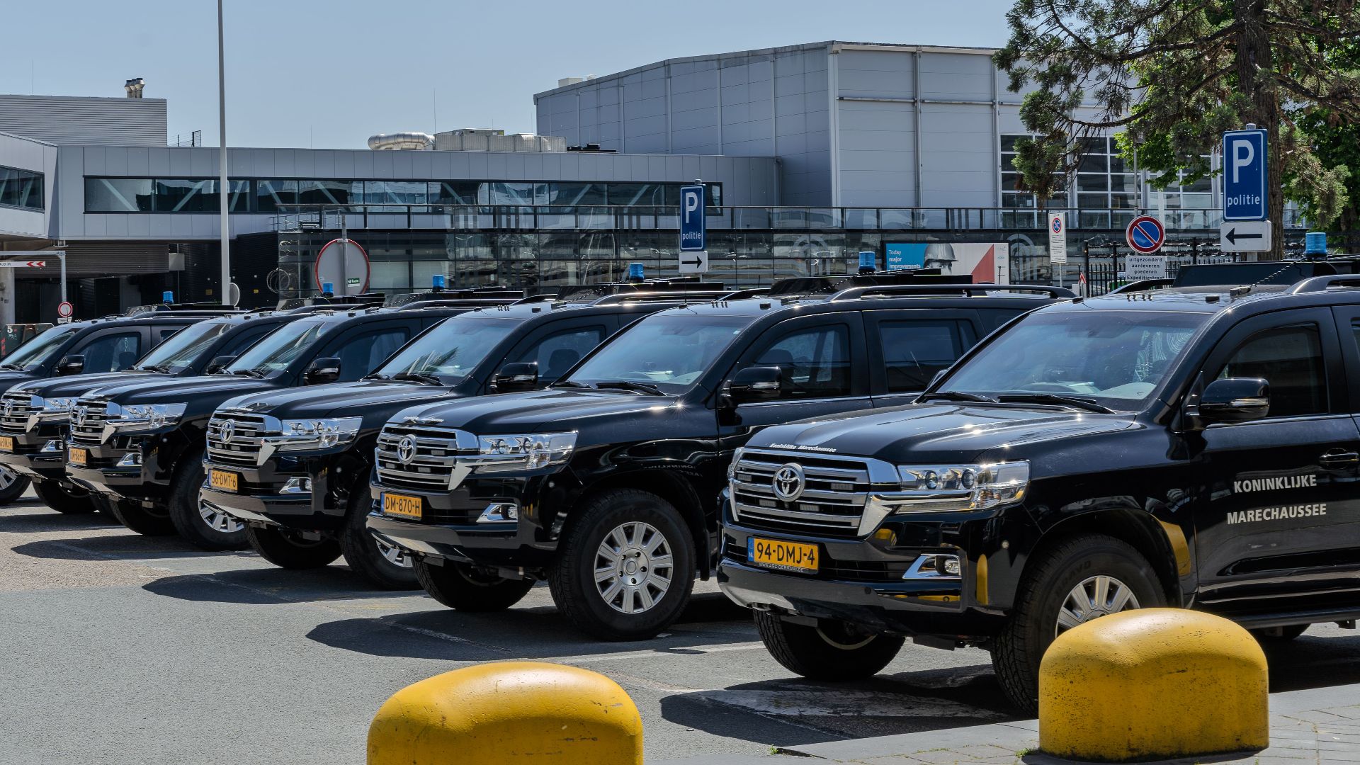 Black SUV police vehicles lined up at an airport parking area under clear skies.