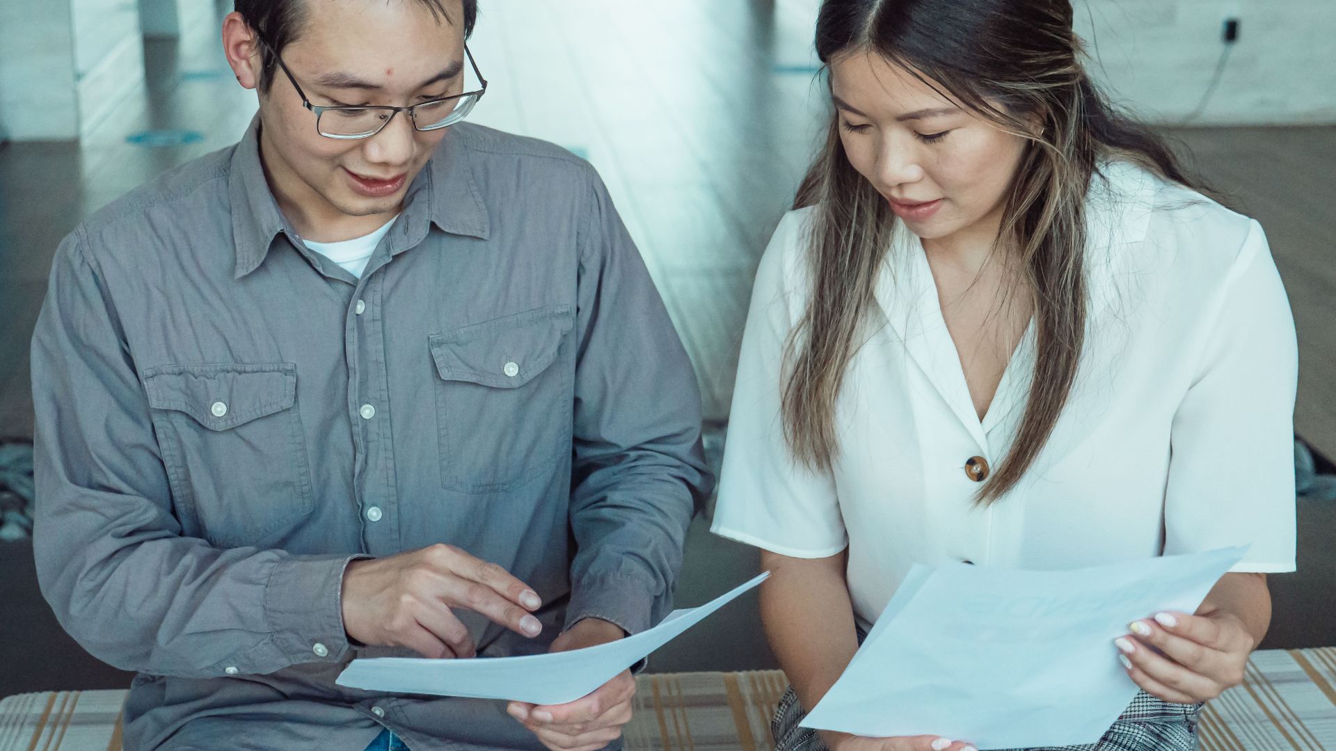 Two coworkers reviewing documents in a modern office, focused on teamwork and planning.
