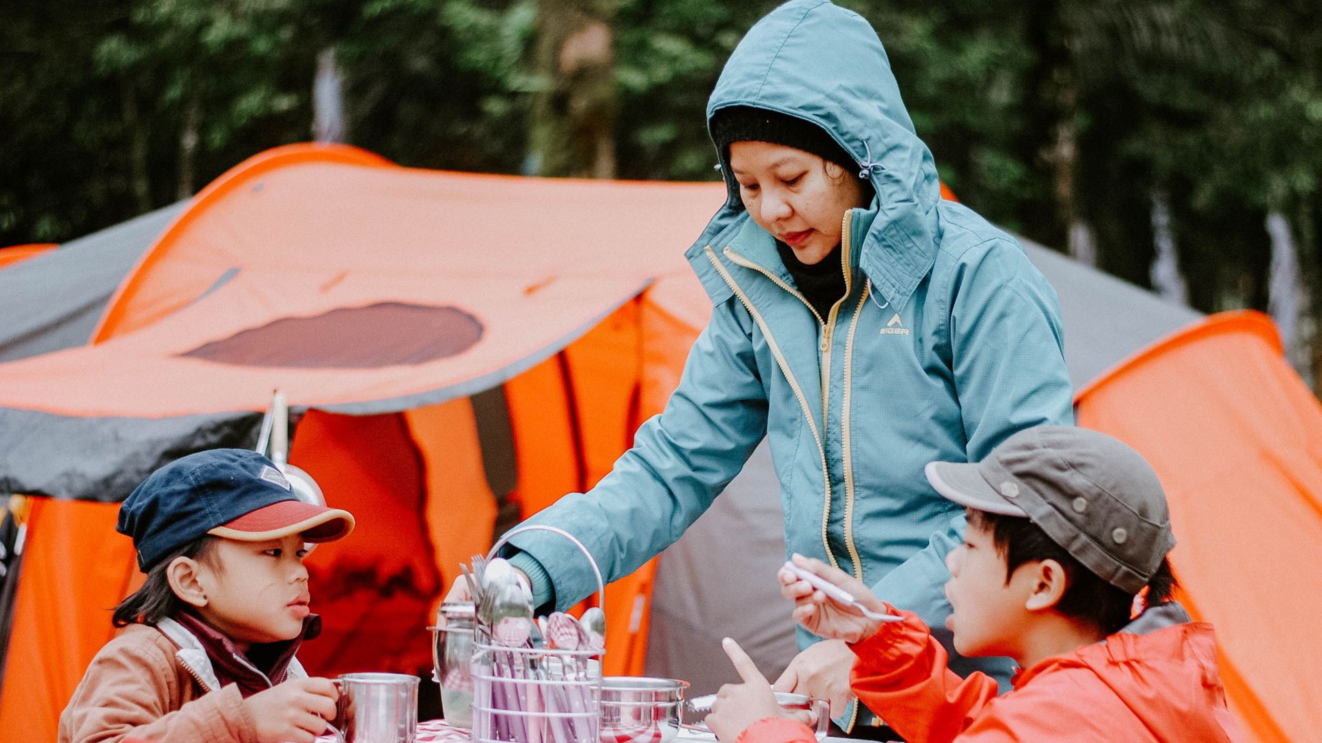 Mother serving food to her children at a campsite with orange tents in the background.
