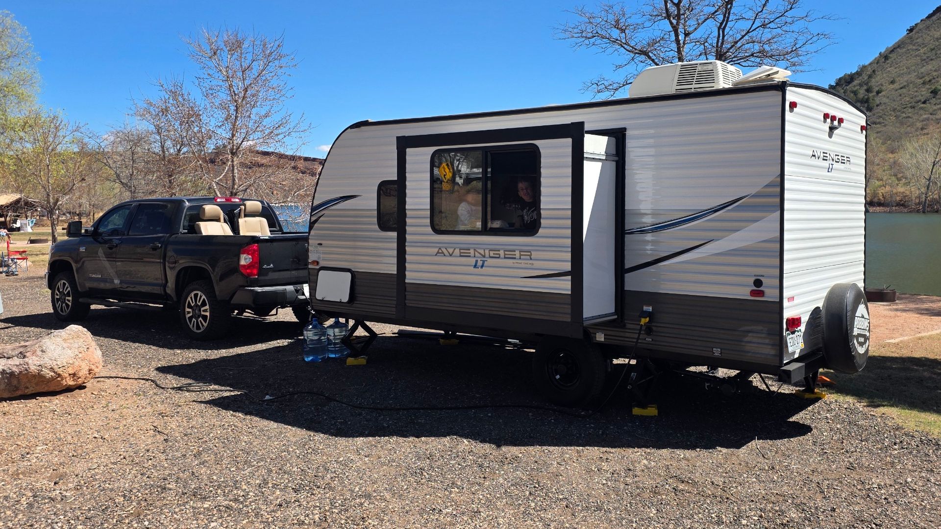 A scenic daytime camping setup with a caravan and truck by a lake in a natural setting.
