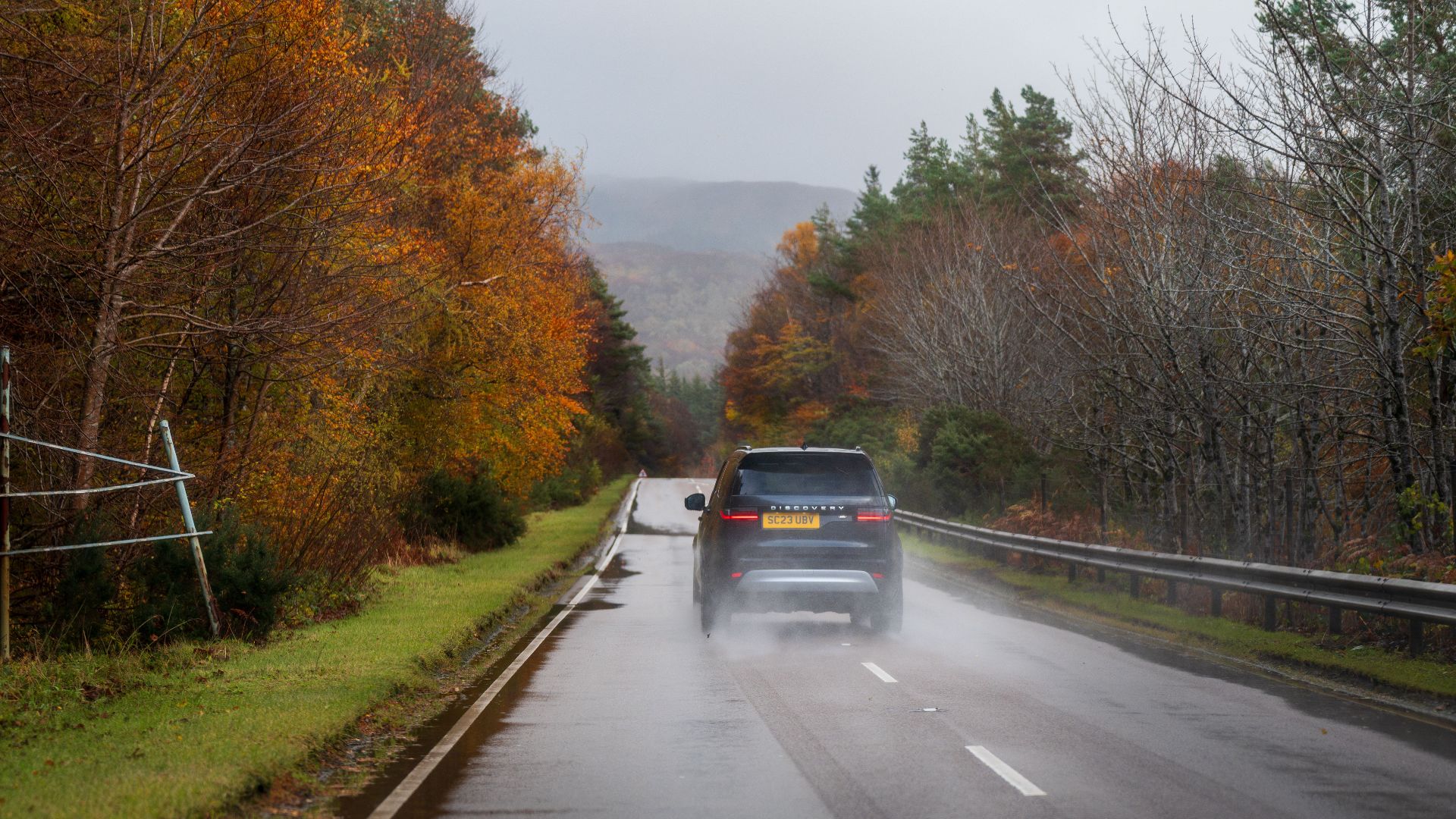 Car driving down a wet road surrounded by colorful autumn trees under a cloudy sky